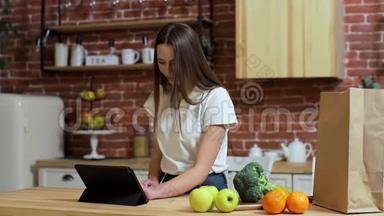 女人在家厨房的<strong>平板</strong>电脑上浏览。 年轻女子在<strong>平板</strong>电脑上浏览，<strong>微笑</strong>着快乐。